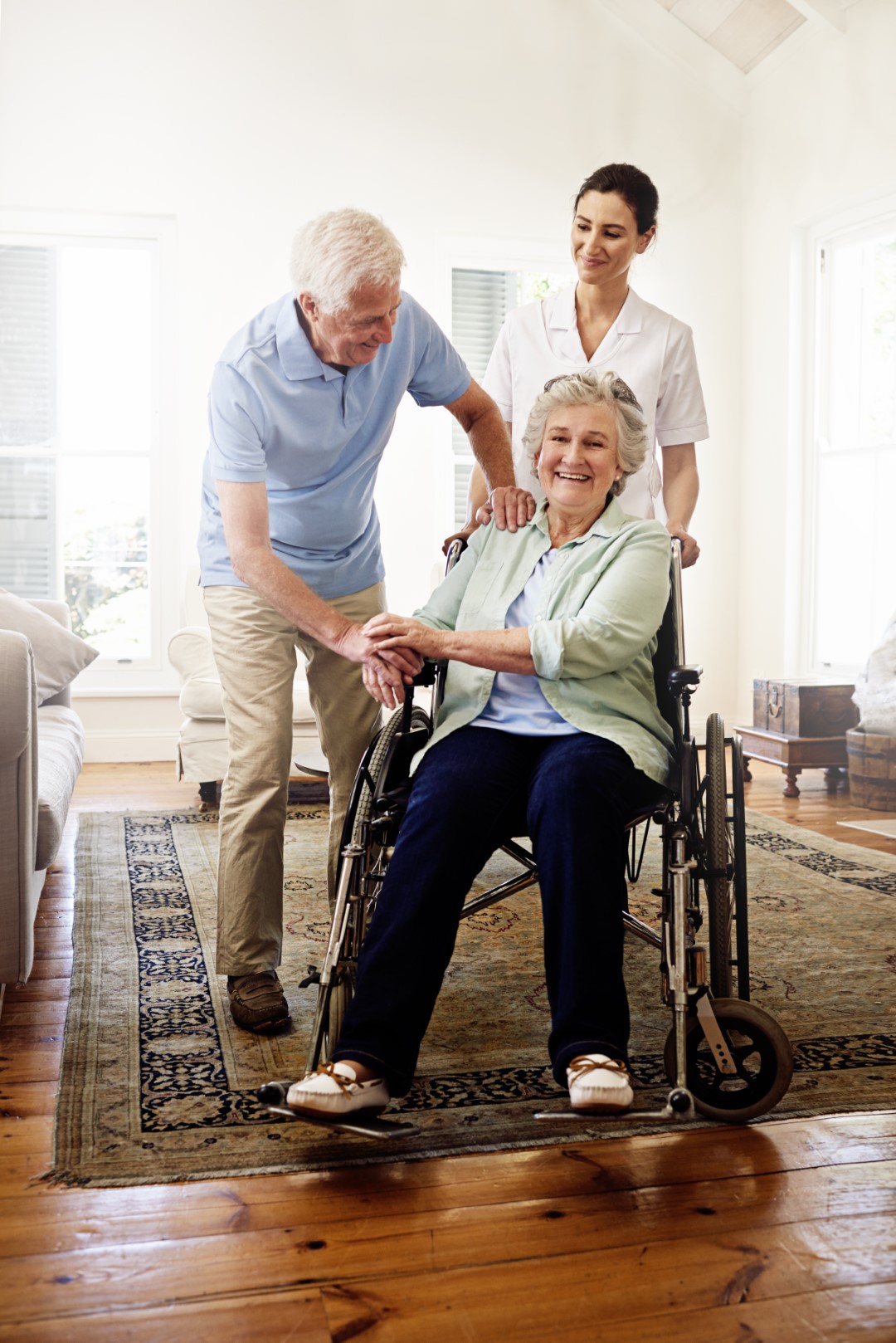 Shot of a smiling caregiver with a senior woman in a wheelchair and her husband at home.